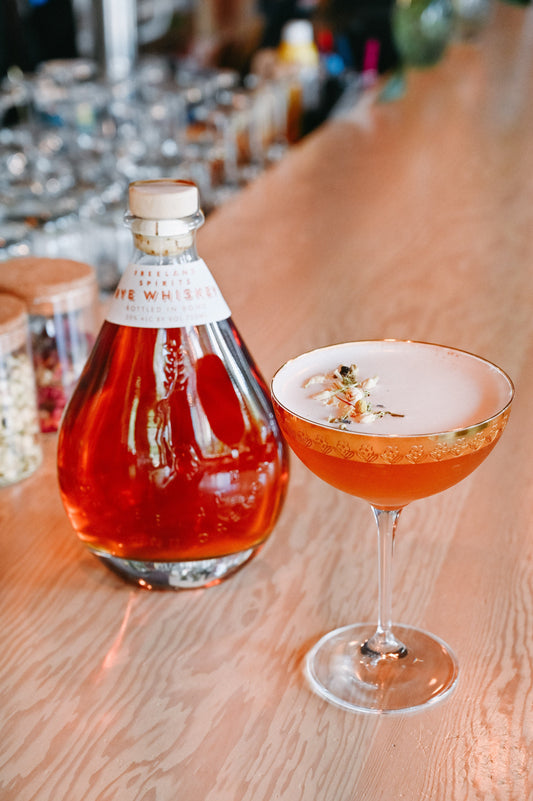 Freeland Spirits limited-release Rye Whiskey, aged for 4 years. Bottle next to Lily of the Valley cocktail, garnished with dried rosebuds.