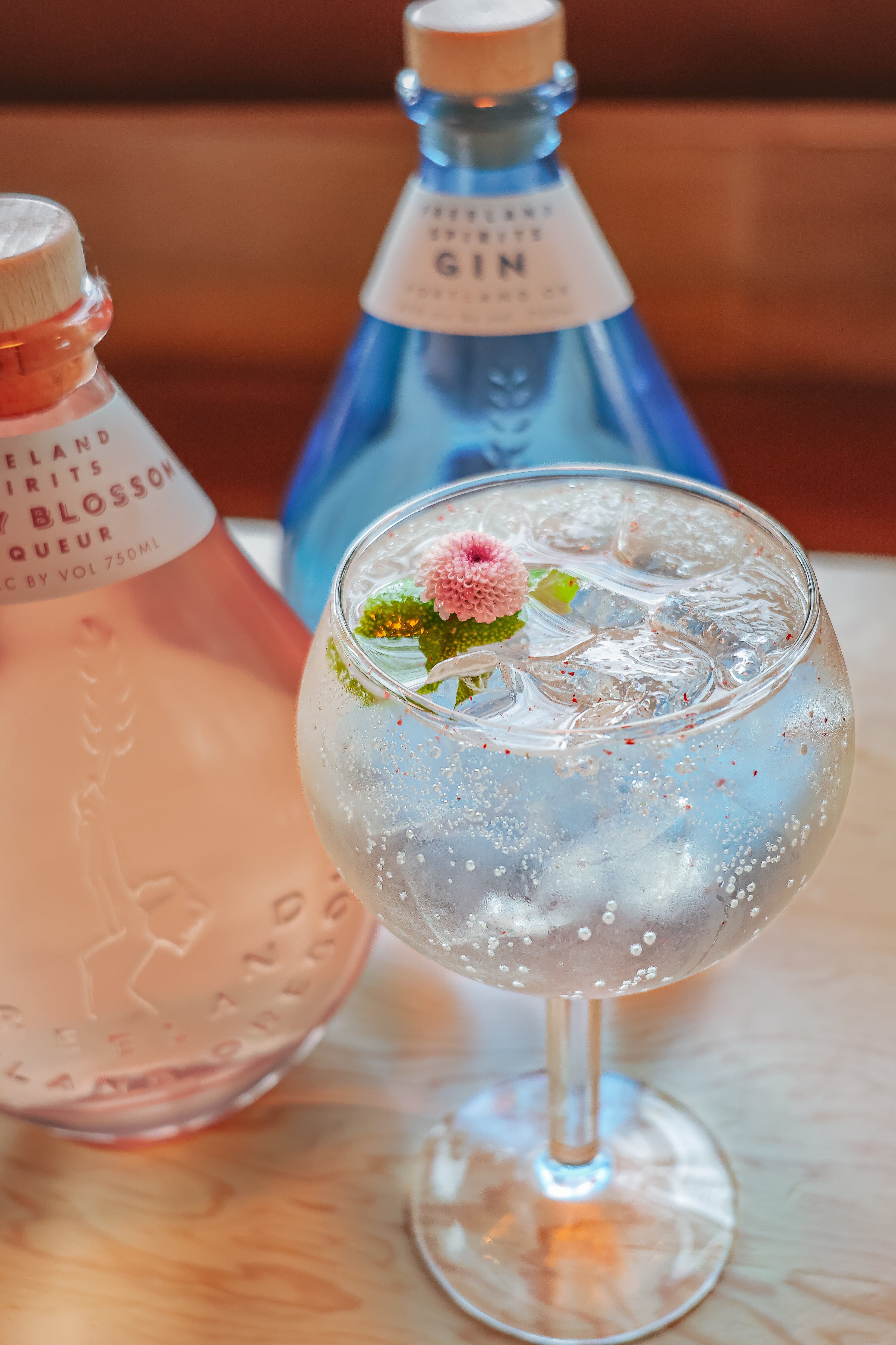 Freeland Cherry Blossom Liqueur and Freeland Gin bottles with a Springtime Gin & Tonic cocktail garnished with a small pink flower
