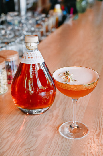 Freeland Spirits limited-release Rye Whiskey, aged for 4 years. Bottle next to Lily of the Valley cocktail, garnished with dried rosebuds. 