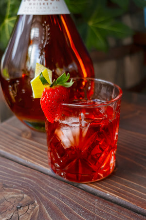 Freeland Spirits Bourbon next to Lover Boy Pride cocktail (a strawberry boulevardier) garnished with strawberry and lemon