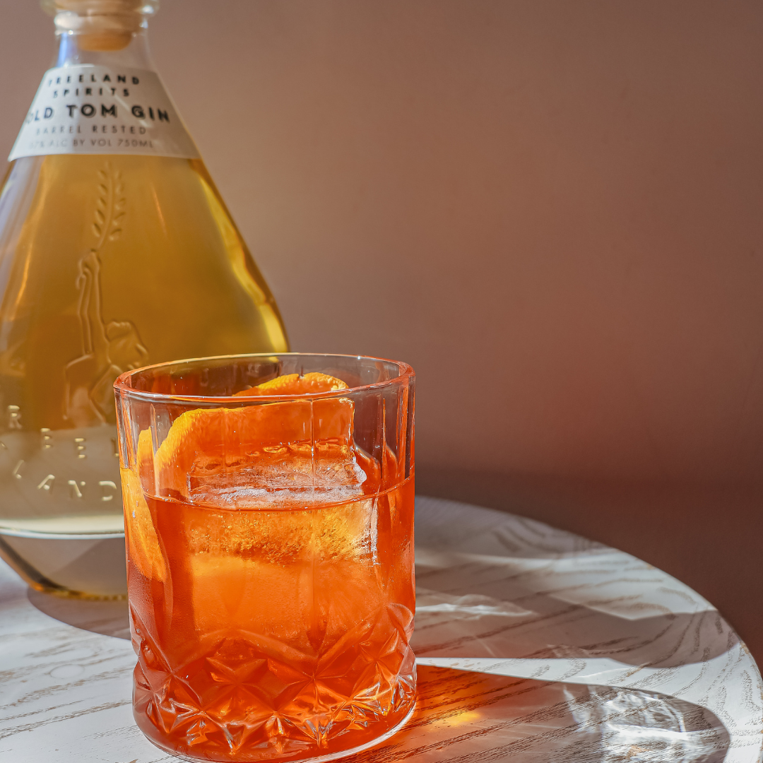 bottle of Freeland Old Tom Gin next to glass of an Old Fashioned made with gin, garnished with orange peel