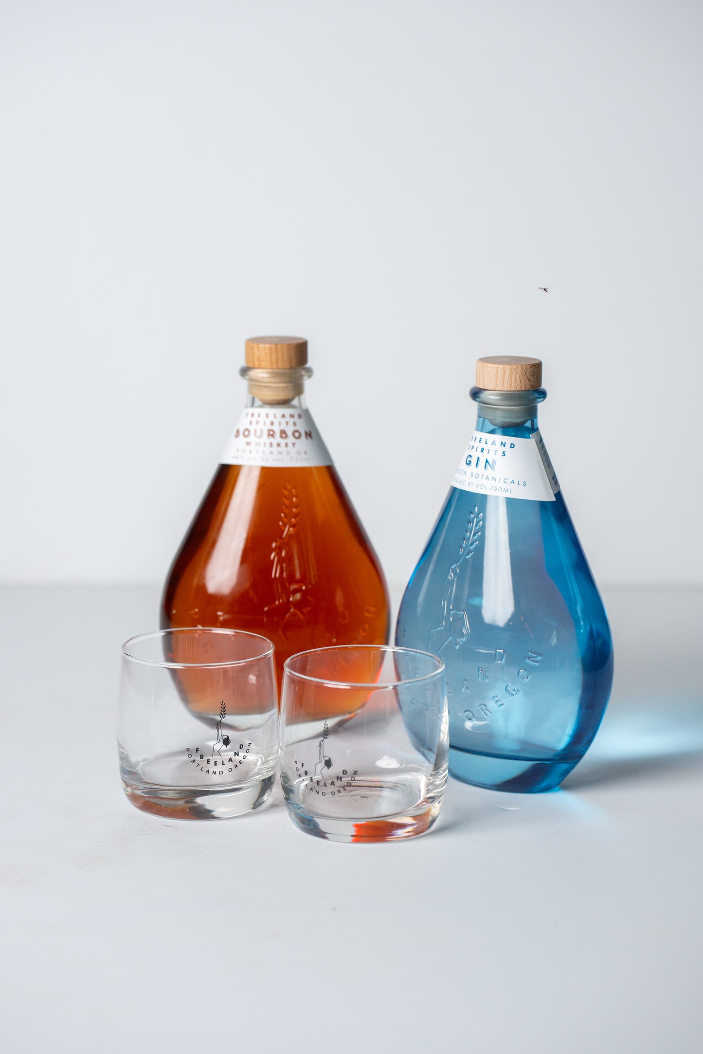 Bottle of Freeland Bourbon whiskey and Freeland Gin, next to pair of branded rocks glasses
