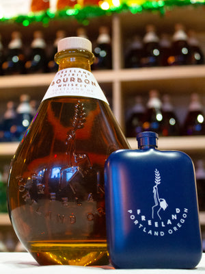 Freeland Spirits branded flask barware next to bottle of Freeland Bourbon